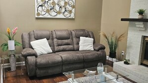 A living room with a brown sofa, a glass coffee table, and a white fireplace. - Charming 3-bedroom house in awesome Urbandale! (Urbandale)