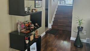A hallway with a wooden floor, a black console table with various items, a potted plant, and a staircase leading to a balcony. - Charming 3-bedroom house in awesome Urbandale! (Urbandale)