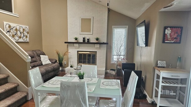 A living room with a fireplace, a dining area with a glass table, and a staircase. - Charming 3-bedroom house in awesome Urbandale! (Urbandale)