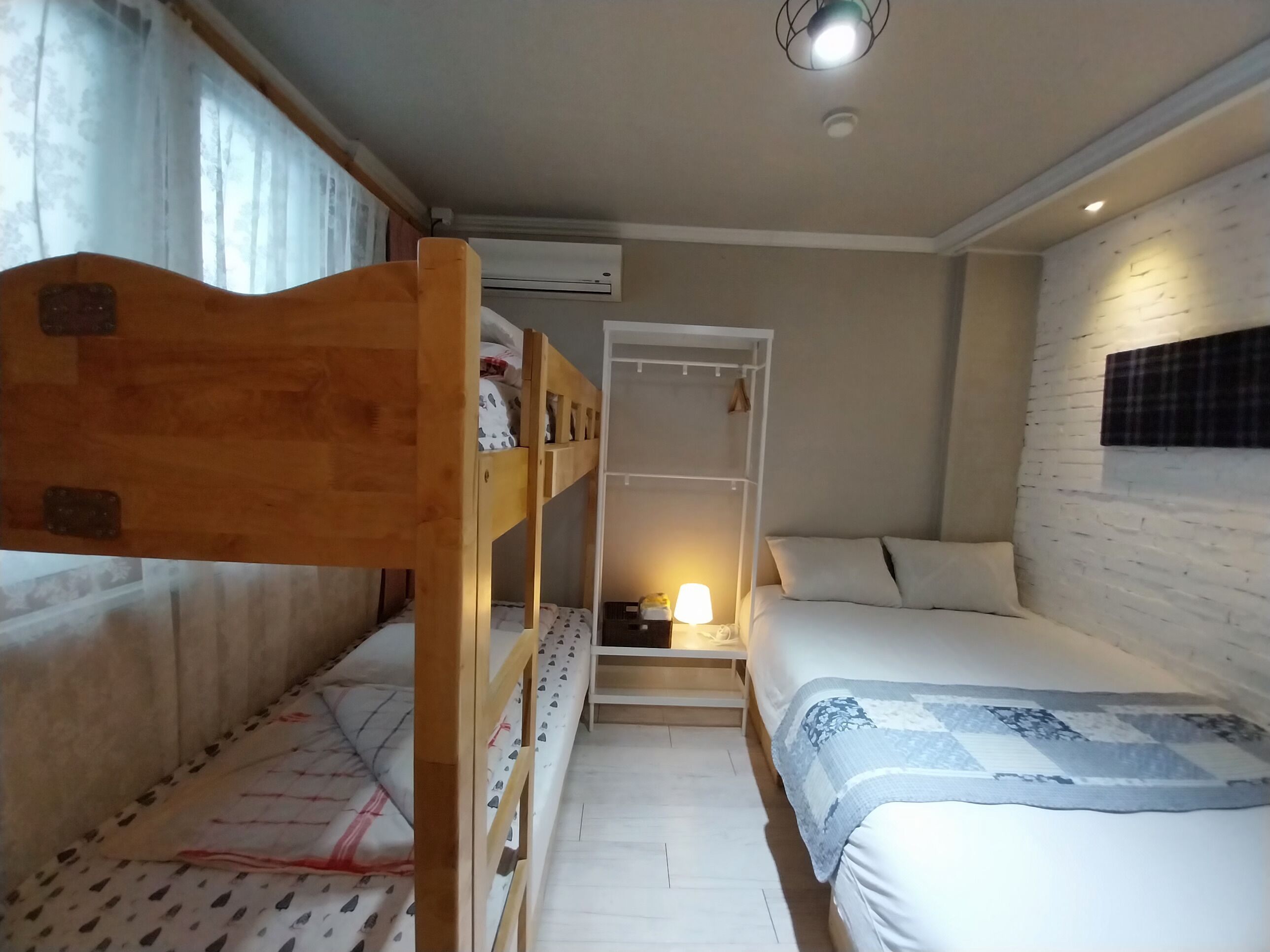 Een kamer met stapelbedden, een nachtkastje met lamp, een kledingkast en een raam met gordijnen.