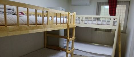 A dormitory room with bunk beds, a ceiling light, an air conditioning unit, and a window with curtains.