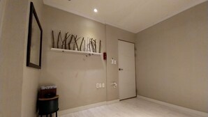 A hallway with a wooden floor, a door, a wall-mounted shelf with branches, and a small table with a basket. - Youngil Dae Guest house (Pohang)