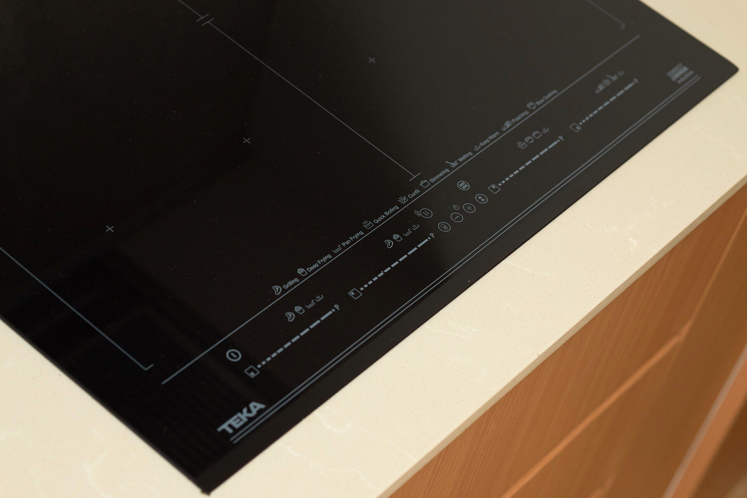 A black induction cooktop with a control panel, a white countertop, and a wooden cabinet.