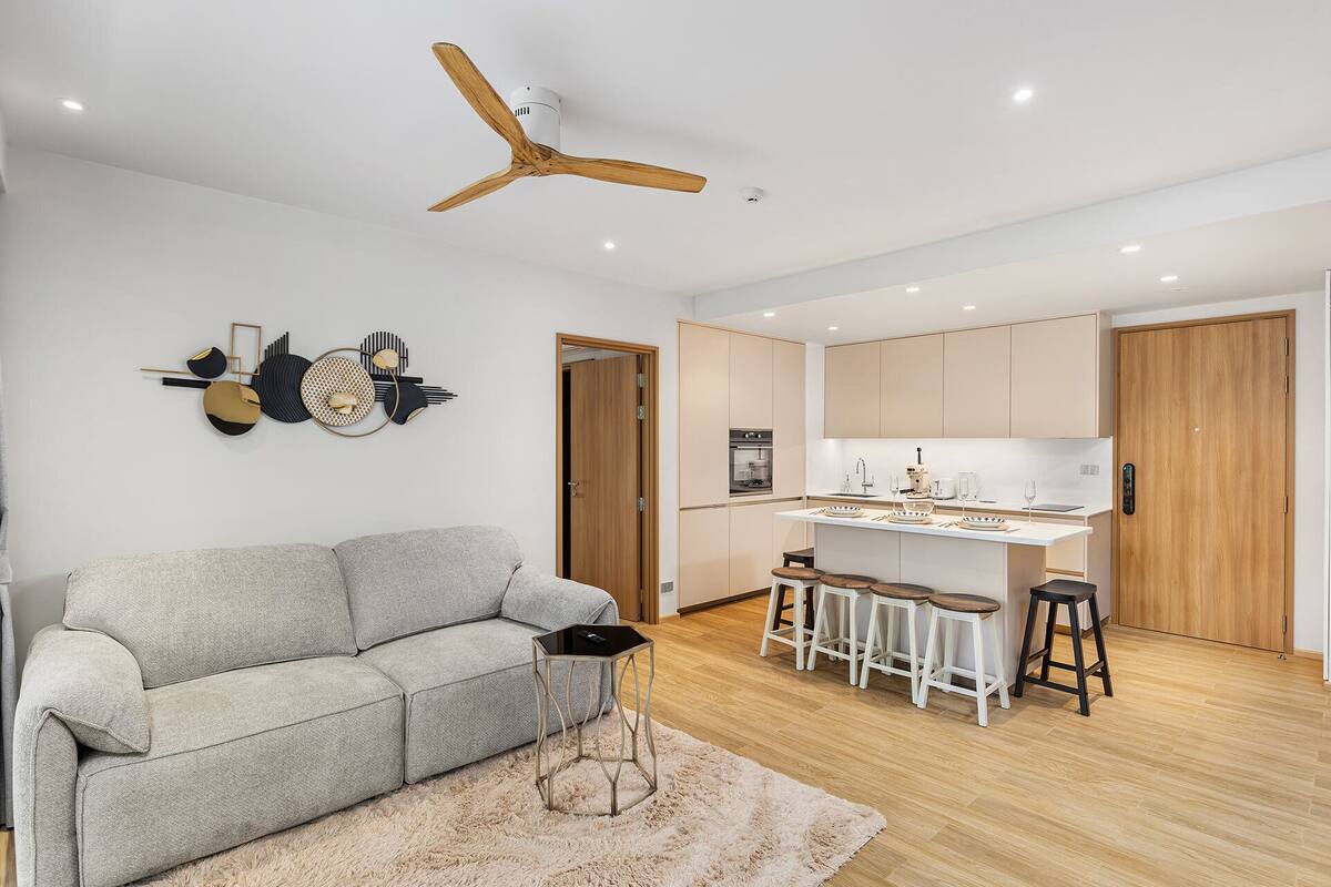 Une cuisine moderne avec un îlot central, un ventilateur de plafond en bois et un canapé gris dans l’espace salon.