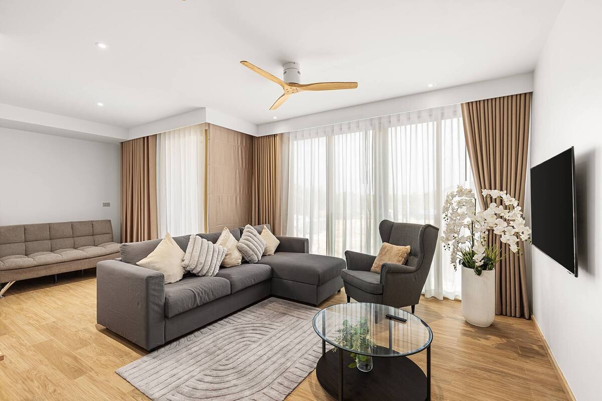 Un salon moderne avec un canapé d’angle, une table basse ronde et un ventilateur de plafond.