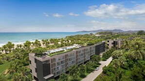 Un hotel moderno con piscina, rodeado de palmeras y vistas a la playa.