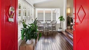 Una habitación con piso de madera, una pequeña mesa redonda con sillas y una ventana con persianas.