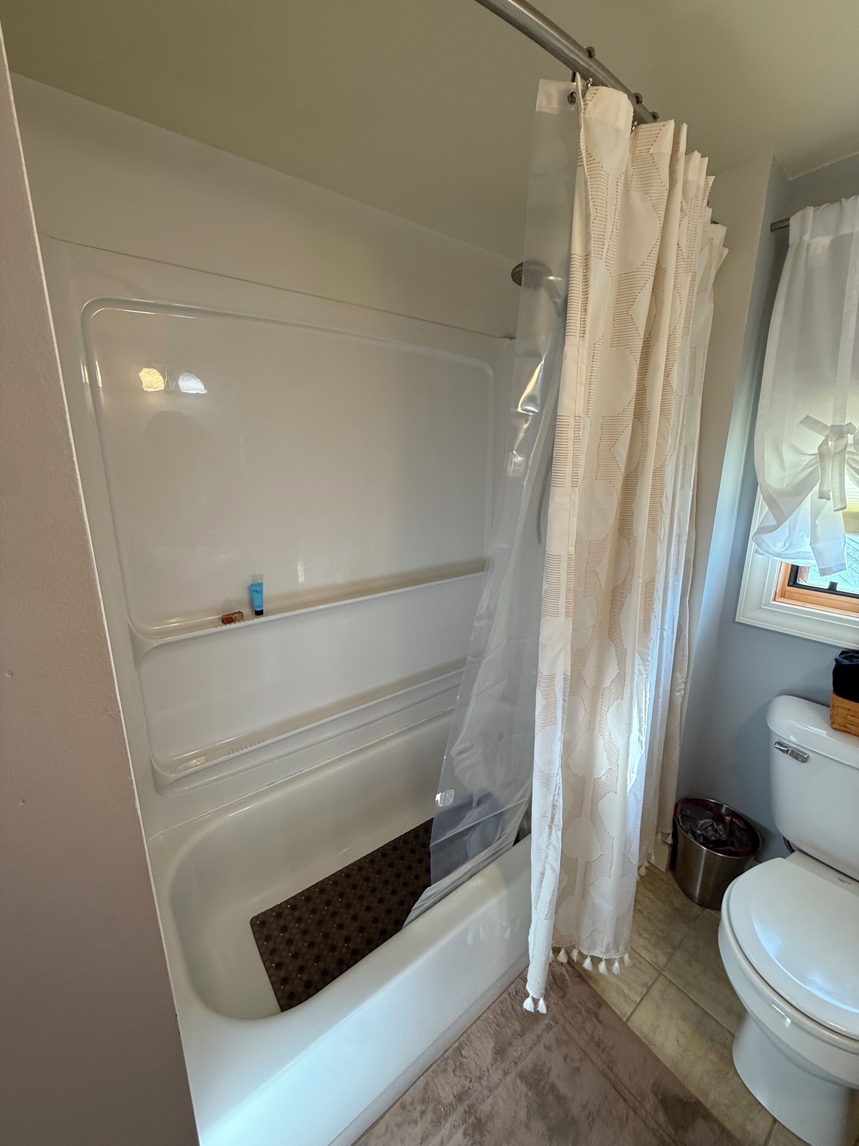 A bathroom with a bathtub, toilet, and a window with a curtain.