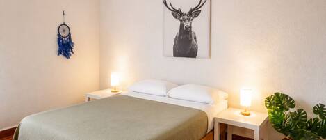 A hotel room with a bed, two bedside tables with lamps, a dreamcatcher, a framed deer picture, and a potted plant.