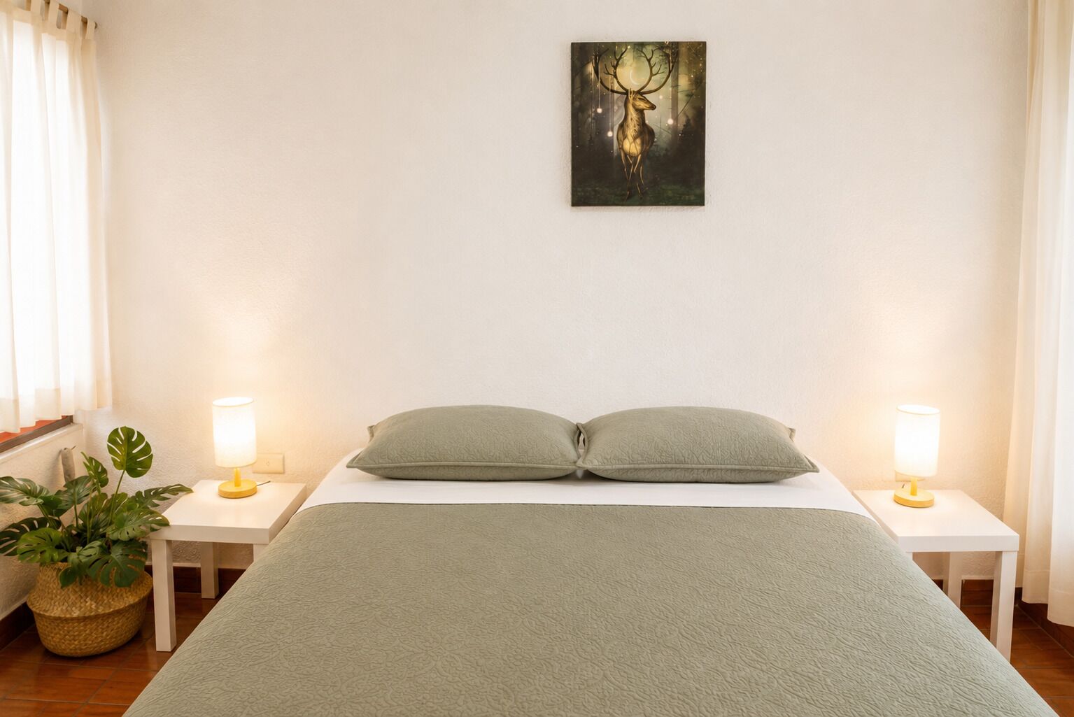 A bedroom with a bed, two bedside tables, a lamp on each side, a wall-mounted painting, and a potted plant.