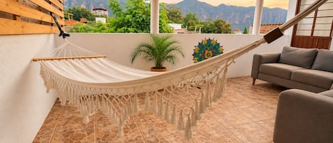 A hammock in a room with a view of mountains, a sofa, and a potted plant.