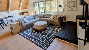 A spacious loft with a large L-shaped sectional sofa, a round ottoman, and a black and white patterned rug. - Harbor Springs Escape, renovated chalet that sleeps 6, near Nubs & Boyne. (Harbor Springs)