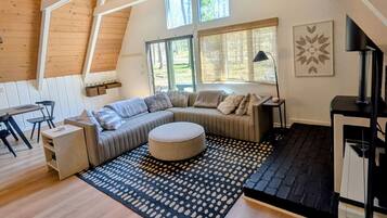 Een ruime loft met een grote L-vormige zithoekbank, een rond ottoman en een zwart-wit vloerkleed.