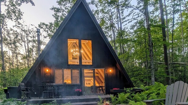 A cabin with a fire pit in front, surrounded by rocks and greenery. - Harbor Springs Escape, renovated chalet that sleeps 6, near Nubs & Boyne. (Harbor Springs)