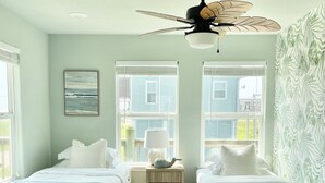 Ein Schlafzimmer mit zwei Betten, einem Deckenventilator, einem Nachttisch und einem Fenster mit Jalousien.