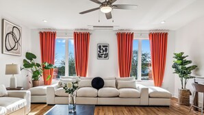 A modern living room with a beige sofa, a coffee table, and a large window with orange curtains. - Nashville Rooftop Oasis! 8 min Broadway. Sleeps 12 (Nashville)