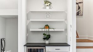 A modern kitchen with white cabinetry, a black countertop, and a built-in oven. There are two white shelves above the countertop, each holding a potted plant. - Nashville Rooftop Oasis! 8 min Broadway. Sleeps 12 (Nashville)