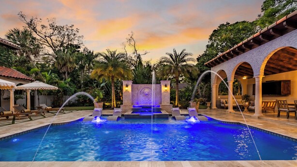 A swimming pool with a water fountain, surrounded by palm trees and a sunset sky. - Full Mediterranean Botanical Garden Estate: 2 Adjacent listings, 9bd 5.5bth EV (Sarasota)