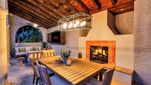 A cozy outdoor dining area with a wooden table and benches, a fireplace, and a Netflix sign. - Full Mediterranean Botanical Garden Estate: 2 Adjacent listings, 9bd 5.5bth EV (Sarasota)
