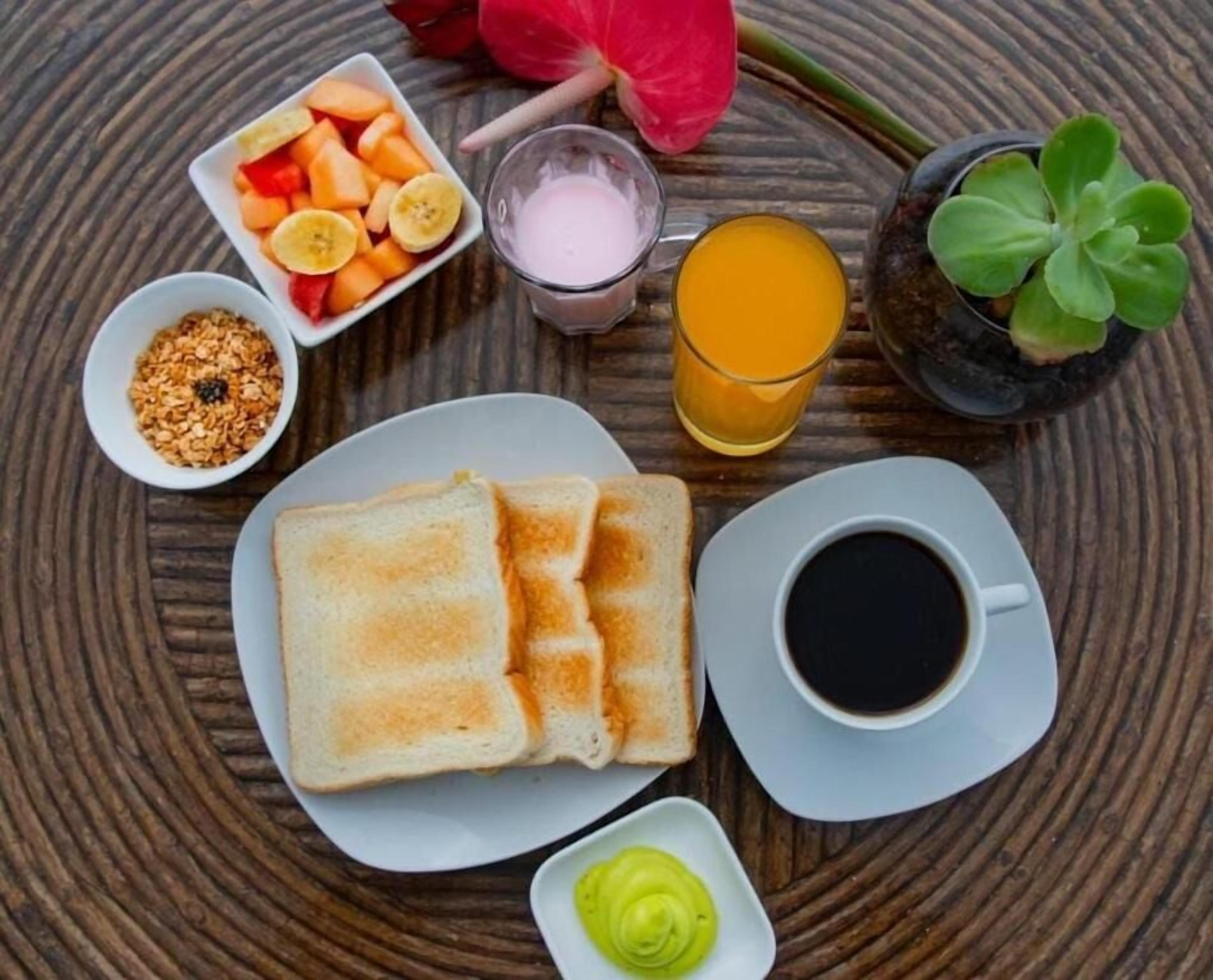 Desayuno con tostadas, fruta, jugo, café y condimentos sobre una mesa redonda.
