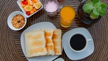 Desayuno con tostadas, fruta, jugo, café y condimentos sobre una mesa redonda.