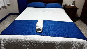 A neatly made bed with blue and white bedding, a wooden headboard, and a small bedside table with a lamp.