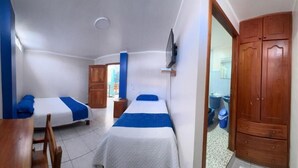 A room with two single beds, a wooden desk, a television, and a wardrobe.