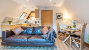Un salon chaleureux avec un canapé en cuir, une table à manger en bois et une cuisine en arrière-plan.