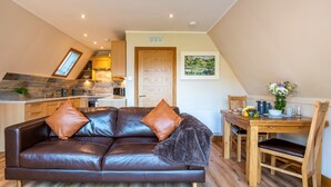 A cozy living area with a leather sofa, wooden dining table, and a kitchen in the background. - Sandpiper Lodge by Interhome (Invergarry)