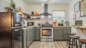 Una cocina moderna con electrodomésticos de acero inoxidable, piso de madera y taburetes de bar.