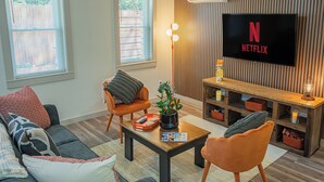 Una sala de estar moderna con un sofá, sillones, una mesa de centro y un televisor mostrando el logotipo de Netflix.