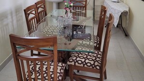 Un coin repas avec une table en verre, des chaises en bois, un évier et un tableau encadré au mur.