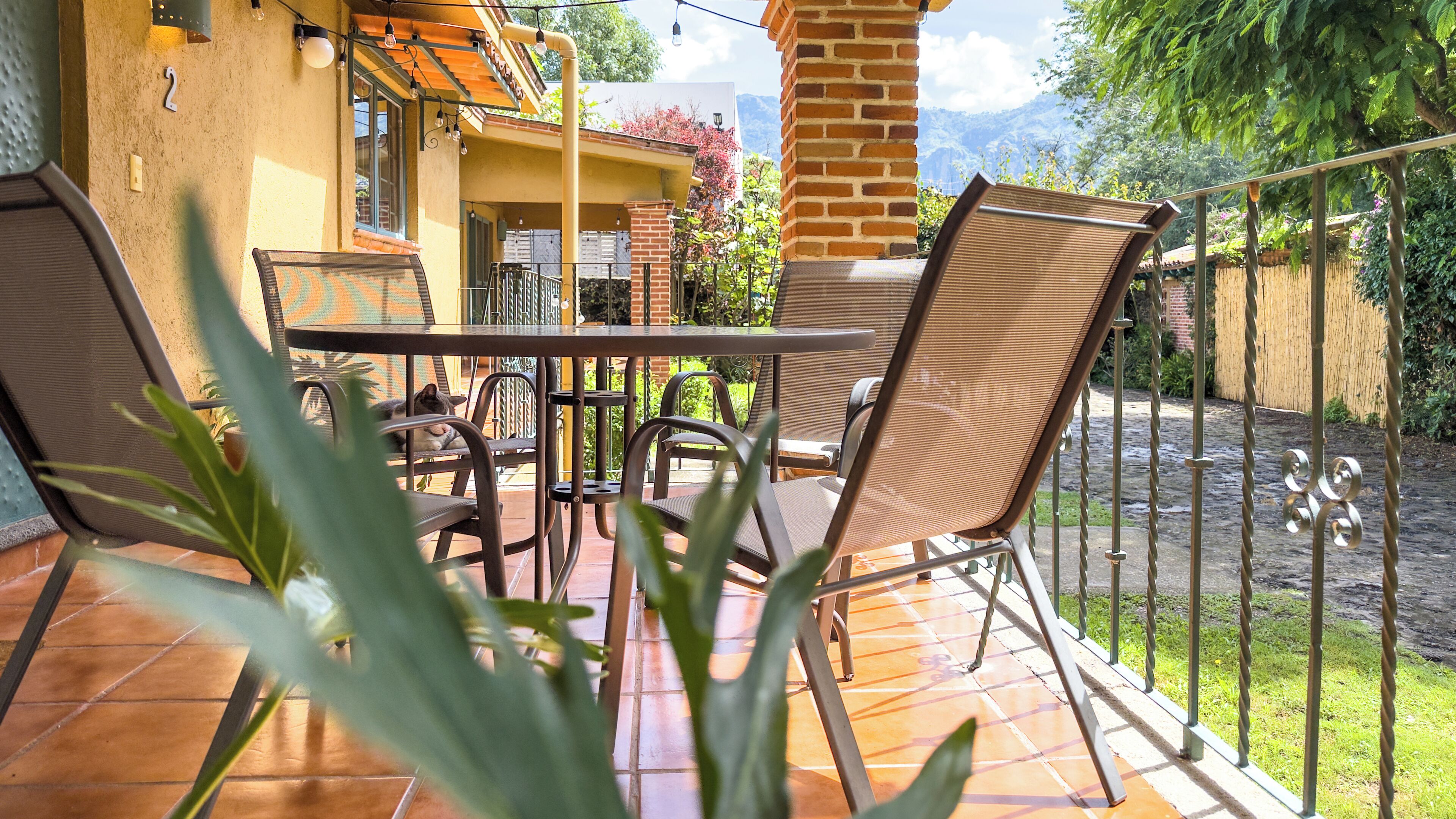 A patio with a table and chairs, a brick wall, and a view of greenery and mountains.