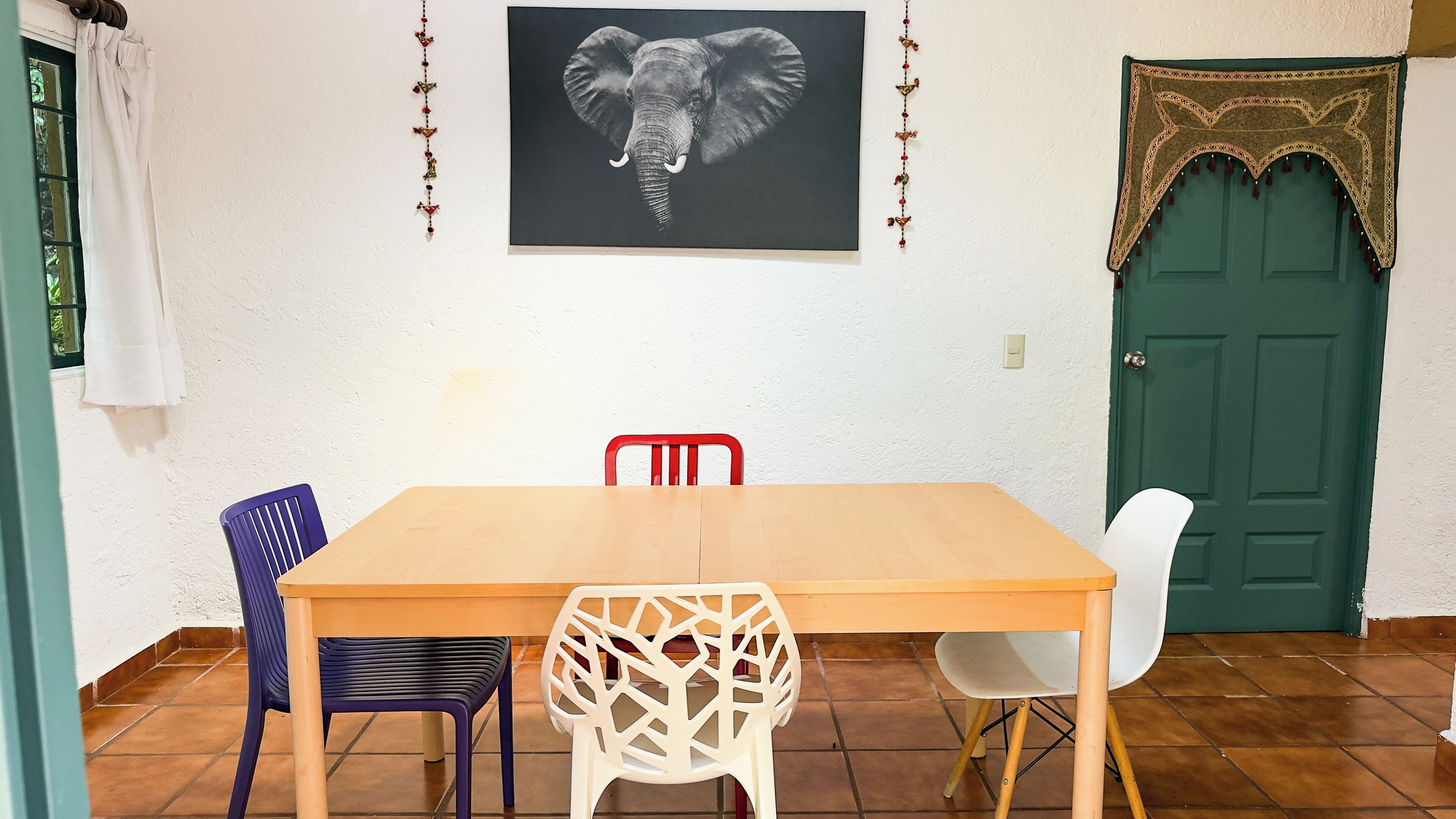 A dining area with a wooden table, two chairs, a decorative wall hanging, and a green door.