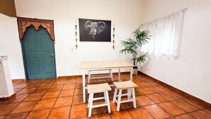 Une pièce avec une porte bleue, un tableau représentant un éléphant encadré, une plante en pot et une table blanche avec des tabourets.
