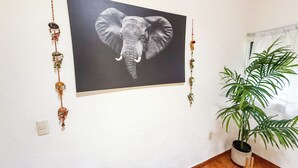 Une pièce avec une œuvre d’art représentant un éléphant accrochée au mur, une plante en pot et un interrupteur mural.