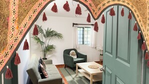 Une pièce comprenant un canapé, un fauteuil, une table, une plante en pot et une porte surmontée d’un arc décoratif.