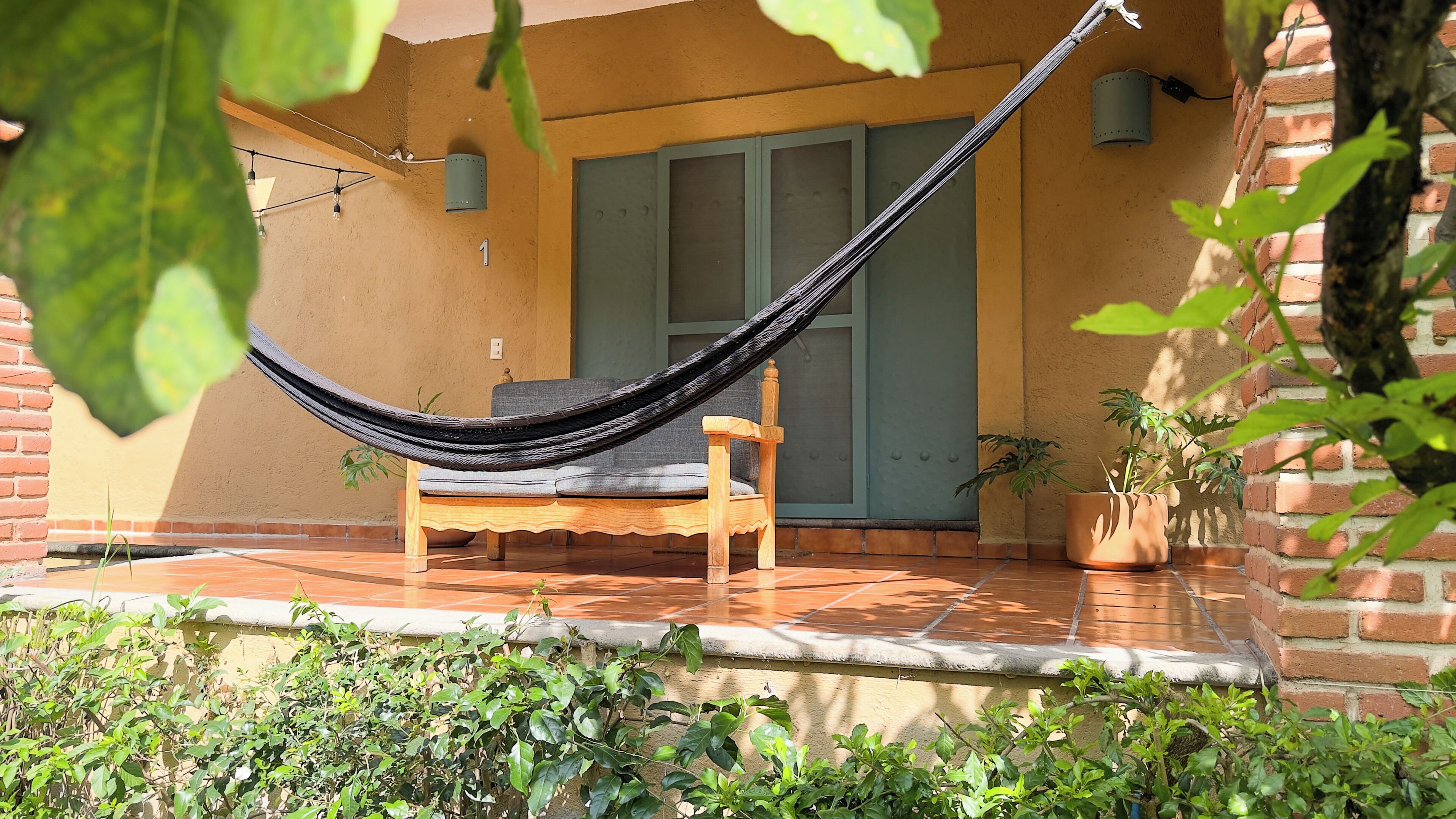 A hammock on a patio with a wooden chair, a potted plant, and a door in the background.