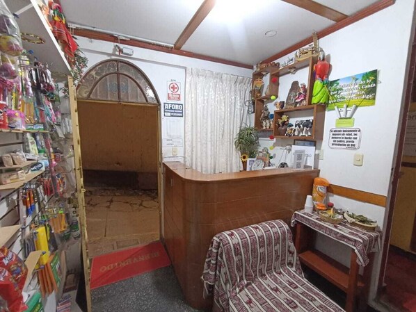 A small, compact room with a reception desk, a patterned sofa, and a shelf with various items. - Hostal Turístico Alborada (Canta)