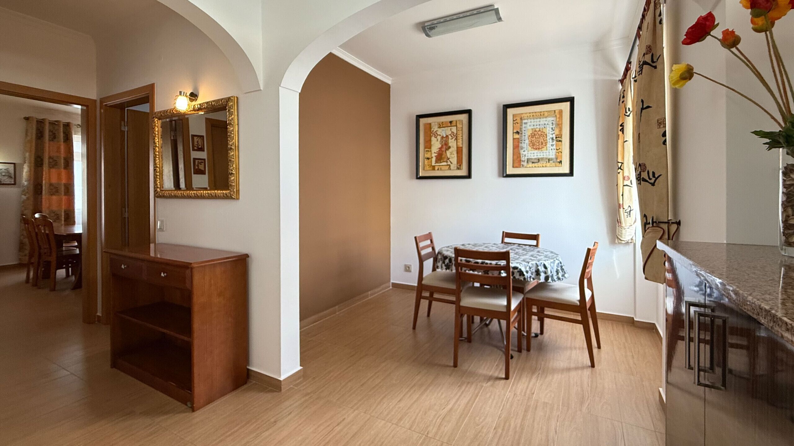Un comedor con una mesa y sillas de madera, un mueble de madera y dos obras de arte enmarcadas en la pared.