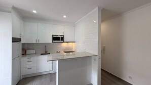 A modern kitchen with white cabinetry, a microwave, and a sink.