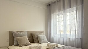 A bedroom with a bed, bedside tables, a window with curtains, and a view of the outside.