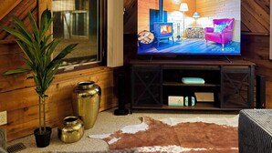 Una sala de estar acogedora con una amplia televisión de pantalla plana, paredes de madera, un ventanal y un tapiz de cuero de vaca.