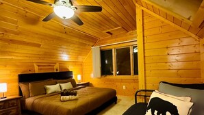 Un dormitorio de cabaña de madera con cama, una silla, una ventana y un ventilador de techo.
