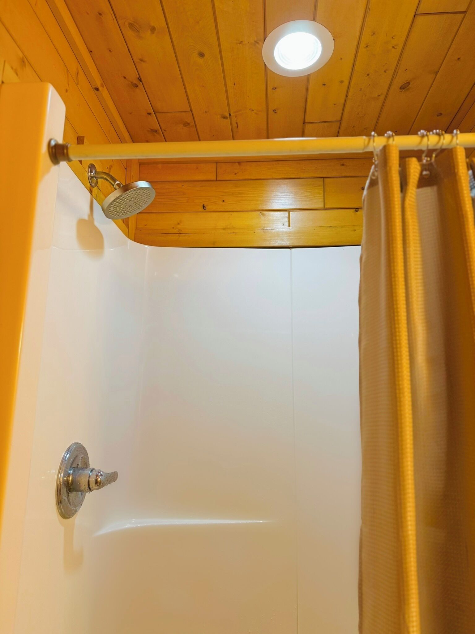 A wooden ceiling with a recessed light fixture, a shower with a handheld showerhead, and a curtain.