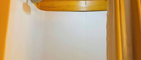 A wooden ceiling with a recessed light fixture, a shower with a handheld showerhead, and a curtain.