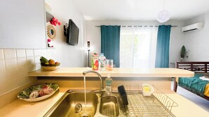 A kitchen with a sink, a dish rack, a fruit bowl, and a window with curtains.