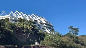 A modern building with a unique geometric roof design, surrounded by lush greenery and palm trees.