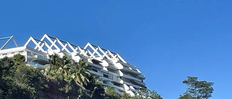 Um edifício moderno com um design geométrico único no telhado, rodeado por vegetação exuberante e palmeiras.