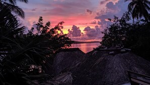 Auringonlaskunäkymä, jossa on penkki ja olkikattoisia rakennelmia.